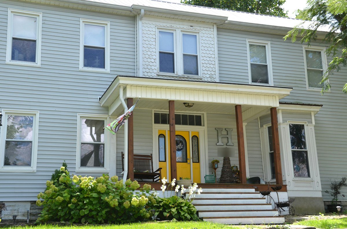 A gray two-story house with a yellow front door and a small porch