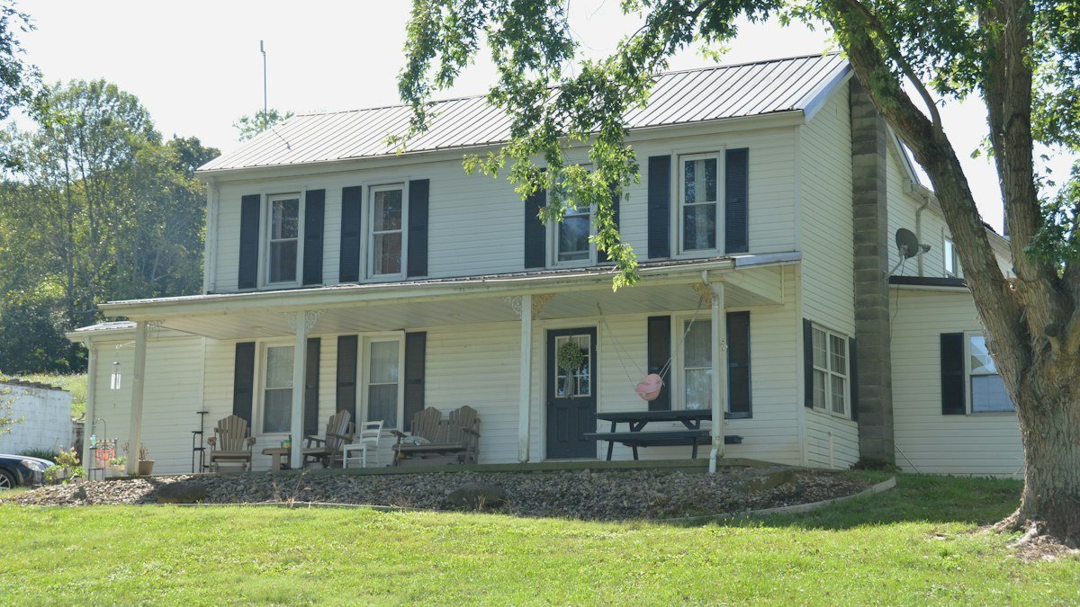 A white two-story farmhouse with a silver metal roof and a long front porch